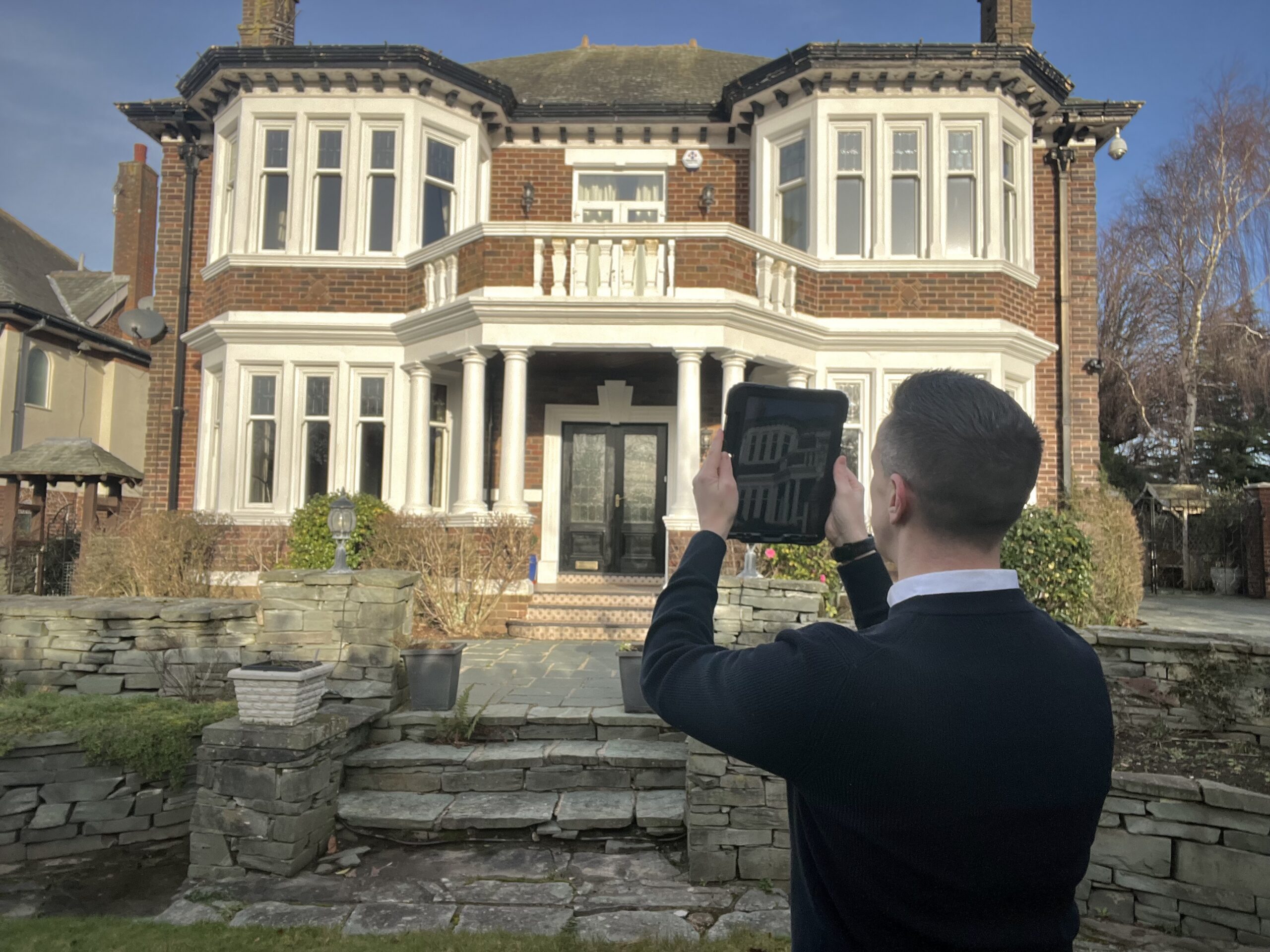 Andrew Raynor, Director of Fylde Coast Chartered Surveyors, taking a photograph of the front of a detached period property